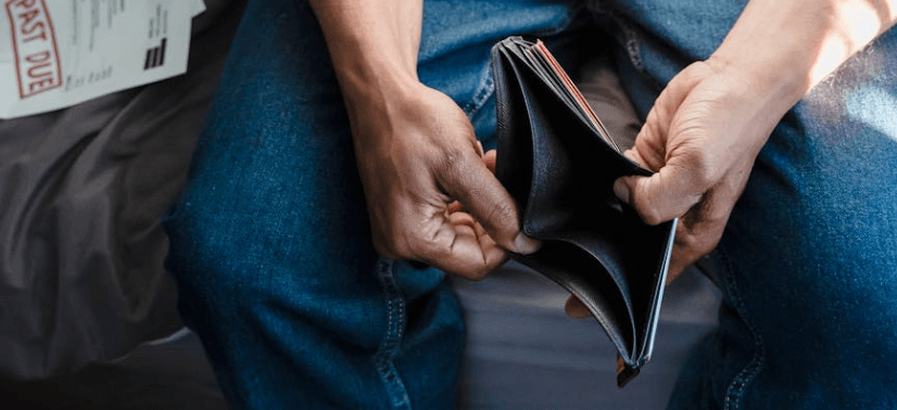 person holding an empty wallet with overdue bills visible in the background