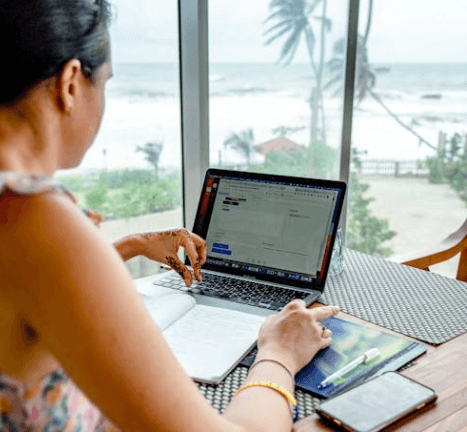 Woman using laptop overlooking beach
