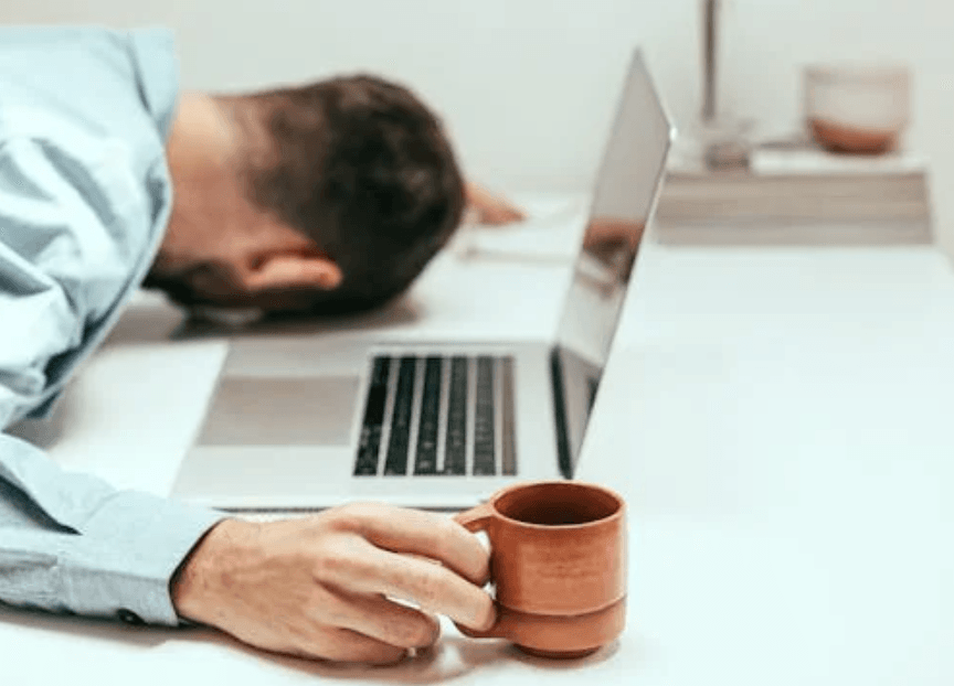 man asleep at computer holding a coffee cup